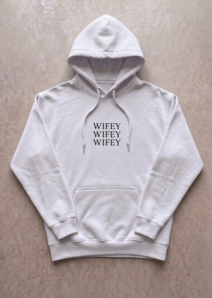 White hoodie with 'WIFEY WIFEY WIFEY' text on a beige background